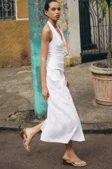 Vestido midi de lino con cuello halter y escote en pico. Presenta un diseño con frunces en el delantero, abertura lateral y cierre posterior con cremallera oculta y botones.