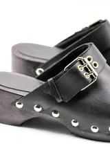 Zuecos negros de cuero vacuno con suela de madera, tachas metálicas y hebilla doble decorativa.