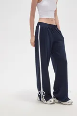 Pantalon deportivo de corte recto y tiro medio, color tostado, con cintura elástica y franjas laterales en tono más claro. Presenta aberturas en los tobillos con cordones ajustables.