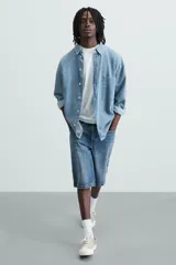 Bermuda de denim de algodón, color azul medio lavado, de corte ancho (baggy fit) y largo hasta la rodilla. Presenta cinco bolsillos y cierre frontal con cremallera y botón.
