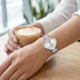 Reloj analógico Mini Focus con caja redonda de metal plateado y malla de acero tipo milanesa. Presenta una esfera minimalista con índices de bastón y números romanos en las posiciones 3, 6, 9 y 12.
