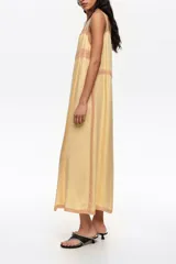 Vestido midi de línea A color amarillo, confeccionado en mezcla de lyocell y viscosa, con botones frontales, escote cuadrado y tirantes finos. Presenta detalles de encaje en contraste y mini tablas verticales en el frente.