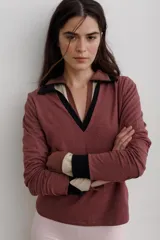 Remera tipo polo de algodón con escote en V profundo y cuello camisero. Presenta un diseño de capas en el cuello y puños, combinando tonos bordó, beige y negro.