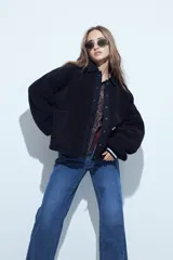 Campera de corderito color marrón oscuro, con cuello camisero y cartera frontal en tela lisa a tono. Presenta cierre mediante botones a presión y mangas largas con puños elásticos.