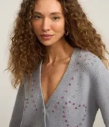 Cardigan corto gris de punto fino, con escote en V, cierre frontal con botones y apliques de pedrería formando corazones.
