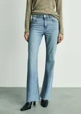 Jeans de denim de tiro medio y corte flare con diseño campana, cinco bolsillos, trabillas para cinturón y bajo deshilachado.