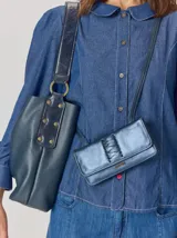 Cartera tipo bandolera de cuero metalizado en tono azulado, con diseño rectangular, solapa con cierre magnético y detalle de trenzado central. Incluye correa regulable y placa metálica con logo.