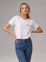Remera blanca de corte cropped con cuello redondo y mangas cortas. Presenta la frase 'SINCE 2024' estampada en color negro en el lado izquierdo del pecho.