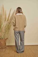 Saco de punto texturizado en color beige, con diseño de cuello redondo, cierre frontal y detalles en contraste de color blanco en los puños y en un bolsillo frontal.