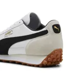 Championes urbanos Puma modelo Easy Rider Mix, color blanco con detalles en negro y beige. Presentan un diseño retro con capellada de cuero y gamuza, logo Puma dorado en el lateral y suela de goma dentada color caramelo.