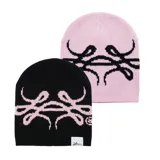 Beanie tejido reversible, con un lado negro y el otro lado rosado claro, ambos con diseño gráfico estampado en contraste.