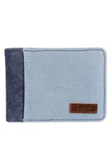Billetera Legacy de lona bicolor, con diseño horizontal, cuerpo principal en color celeste y detalle en el lateral izquierdo en azul marino. Incluye una pequeña etiqueta de cuero marrón con el logo grabado en la esquina inferior derecha.