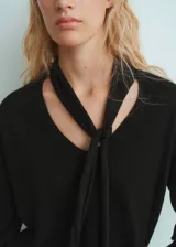 Jersey de punto fino color negro, con cuello en pico y detalle de fular integrado en el escote. Presenta un diseño recto y mangas largas.