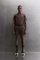 Short de running color marrón, confeccionado en tejido técnico elástico con forro interior. Cuenta con cintura elástica ajustable, bolsillos laterales con cierre de cremallera oculto y aberturas en las perneras.
