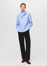 Blusa de manga larga con diseño de rayas verticales en tonos azul y blanco. Presenta un cuello redondo con un pañuelo integrado que cae sobre el pecho y puños abotonados.