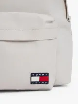 Mochila de diseño redondeado en color gris claro, confeccionada en poliéster texturizado. Cuenta con un compartimento principal con cierre, un bolsillo exterior con cremallera en la parte frontal y un bolsillo interior de malla abierto. Posee asa superior y correas ajustables y acolchadas. Lleva un parche tejido de Tommy Jeans en la parte delantera.