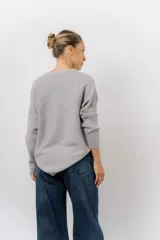 Buzo tejido de punto en color beige, con cuello redondo, mangas largas y silueta relajada con dobladillo irregular, siendo más largo en la parte trasera.