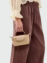 Cartera tipo pouch de la línea Le Pliage de Longchamp, confeccionada en cuero sintético color beige con solapa frontal a tono y cierre de cremallera superior.