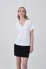 Blusa de poliéster color blanco con cuello en V, mangas cortas con dobladillo y corte holgado.