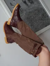 Botas altas de cuero marrón combinadas con gamuza blanca con estampado de vaca, forradas en cuero y con cierre de bronce.