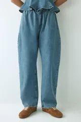Pantalón oversized en denim de algodón rígido, con elástico revestido en la cintura, cierre con botón y bolsillos laterales discretos. Presenta un corte con piernas de diseño curvo y volumen.