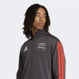 Campera deportiva Adidas de cuello alto y cierre frontal, confeccionada en tejido de tricot. Presenta diseño en color gris oscuro con las icónicas tres tiras en color rojo a lo largo de las mangas, logo de la marca en el pecho y emblema del equipo Audi Revolut F1 Team. Incluye bolsillos laterales.