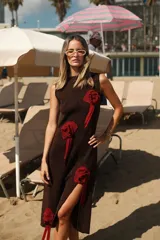 Vestido midi marrón de lurex, con cuello redondo y sin mangas. Presenta apliques de rosettes rojas en el frente y tajo lateral.