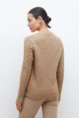 Sweater color beige melange de tejido de punto con diseño de trenzas y detalles de perlas en el frente y las mangas.