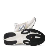 Championes urbanos New Balance modelo Amaste, con diseño en tonos beige y blanco, detalles en azul y rojo en la lengüeta, y el logo característico en el lateral.