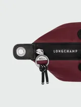 Cartera de mano modelo Le Pliage Energy de Longchamp, tamaño pequeño. Confeccionada en lona de color bordó con detalles en cuero negro, incluyendo solapa frontal con cierre de botón a presión y asas cortas. Incluye correa de hombro ajustable y extraíble de tejido técnico negro.