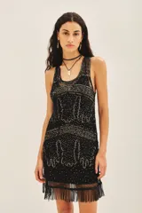 Vestido corto negro de calce recto, sin mangas y escote redondo. Confeccionado en tul bordado con piedras, lentejuelas, canutillos y flecos de mostacillas. Incluye un viso a tono con breteles finos.