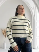 Sweater de punto grueso color crema con cuello alto y rayas horizontales negras. Tiene roturas en el ruedo.