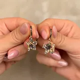 Aros tipo argolla con dije colgante en forma de estrella, decorados con cristales en tonos negros, dorados y plateados.
