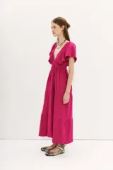 Vestido midi de color fucsia, con escote en V profundo, mangas cortas amplias y cintura elastizada. Presenta una falda con caída fluida y espalda cuadrada.