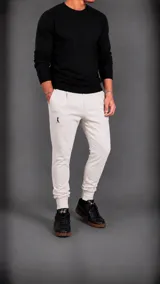 Pantalón tipo jogger color beige, con cintura elástica, bolsillos laterales y puños ajustados en los tobillos. Presenta un pequeño logo bordado en la parte superior del muslo derecho.