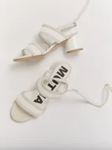 Sandalias de tacón redondo de 6 cm, con diseño de tiras translúcidas de TPU y detalles en gamuza. Cuentan con cierre de pulsera ajustable al tobillo.