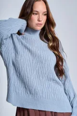 Sweater color crema con cuello alto y diseño de trenzas.