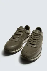 Zapatilla deportiva color verde militar, con parte superior de múltiples piezas que combinan piel y serraje. Presenta horma redonda y suela dentada en color crema con base marrón.