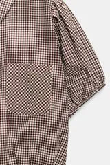 Camisa corta de cuello solapa y manga corta abullonada acabada en elástico, color verde con estampado de cuadros vichy. Cuenta con un bolsillo de plastrón en el delantero, bajo con elástico y cierre frontal con botones.