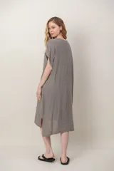 Vestido midi de lino color beige, de corte holgado y silueta acampanada. Cuenta con cuello redondo, mangas cortas amplias, bolsillos laterales y detalles de recortes horizontales en la falda con terminación asimétrica más larga en la parte trasera.