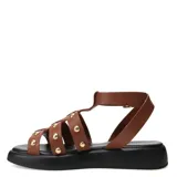 Sandalias estilo gladiador con tiras de cuero color marrón, decoradas con tachas metálicas doradas. Posee una base de plataforma plana color negro y cierre con hebilla ajustable en el tobillo.