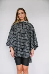 Poncho de paño con estampa a cuadros en tonos grises, negros y blancos, con cuello camisero gris y cierre frontal con dos botones.
