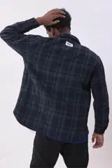 Campera tipo sobrecamisa de franela con diseño a cuadros en tonos beige y marrón. Presenta cuello clásico, cierre frontal con botones, dos bolsillos frontales con solapa y botones en el pecho, y mangas largas con puños abotonados.