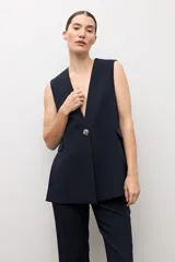 Chaleco largo sastrero de color negro, con escote en V profundo, cierre frontal con un botón metálico y bolsillos laterales con solapa.
