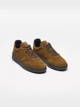 Championes Veja modelo V-90 Suede, confeccionados íntegramente en gamuja de color marrón coñac. Presentan puntera perforada, cordones tono sobre tono, suela de goma marrón y la clásica 'V' de la marca en el lateral con el mismo material y tono. Incluyen detalles de la marca grabados en el talón.