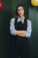 Mono largo de color negro con cierre frontal de botones vintage de distintos colores. Presenta un diseño sin mangas, con bolsillos laterales y una cinta para herramientas en la parte trasera.