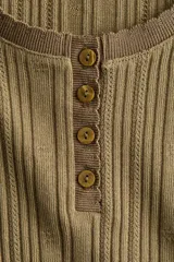 Top de manga larga en punto acanalado de algodón con diseño pointelle, escote en U con ribete festoneado y tapeta con botones frontales.