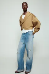 Chaqueta corta de Zara confeccionada en mezcla de algodón, con cuello solapa, manga larga con hombro caído y puños elásticos. Presenta un diseño cruzado con cierre de hebilla metálica lateral y forro interior a tono.
