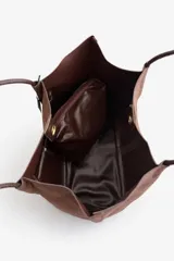 Bolso tipo shopper de material sintético con acabado efecto gamuza en color marrón, con asas largas para llevar al hombro. Incluye un neceser interno de material brillante a tono con cierre metálico.