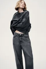 Jean de corte baggy, estilo holgado con piernas rectas, confeccionado en denim de algodón color gris oscuro con efecto lavado. Cuenta con tiro estándar, trabillas para cinto, cierre frontal con botón y cinco bolsillos clásicos.